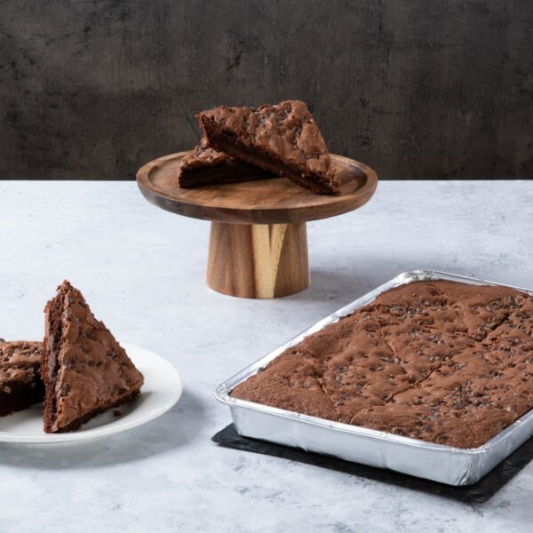 Chocolate cake with creamy frosting and chocolate topping on a wooden board.
