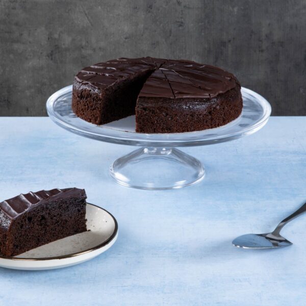 Chocolate cake with creamy frosting and chocolate topping on a wooden board.